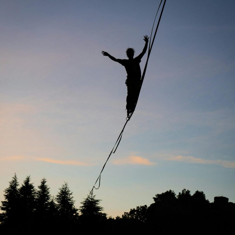 A captivating silhouette of a person balancing on a tightrope during dusk, with trees below.